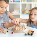 A boy and a girl playing with a Montessori Memory Match wooden game on a table in their room.