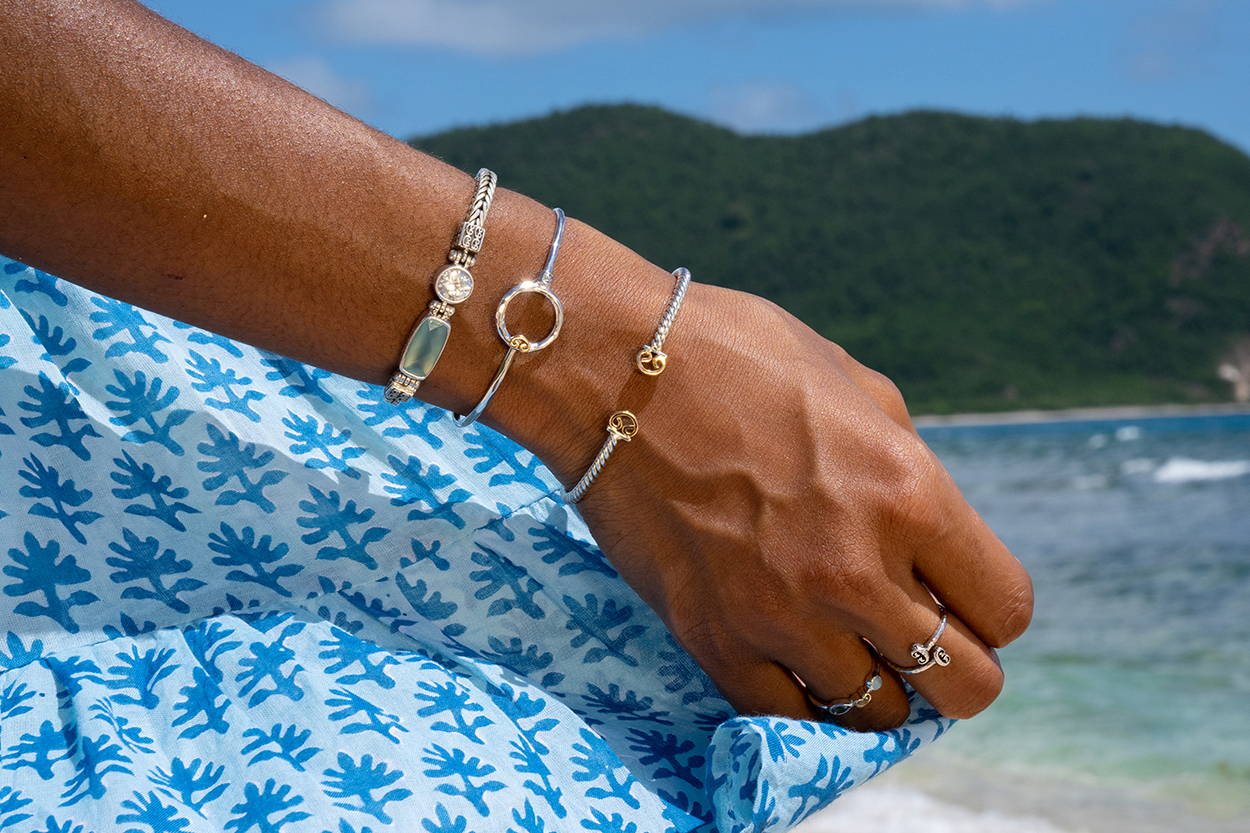 Hand holding a blue dress at the beach wearing Vibe Jewelry.