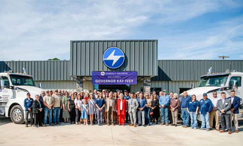 A large, diverse crowd gathers for a celebration with trucks and a banner for "Governor Ken Yeet," conveying unity and optimism.