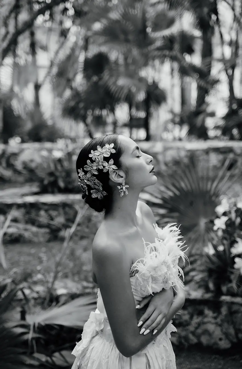 Une belle femme mexicaine aux cheveux noirs coiffés en chignon portant des boucles d'oreilles dorées, une robe blanche et une grande coiffe florale.