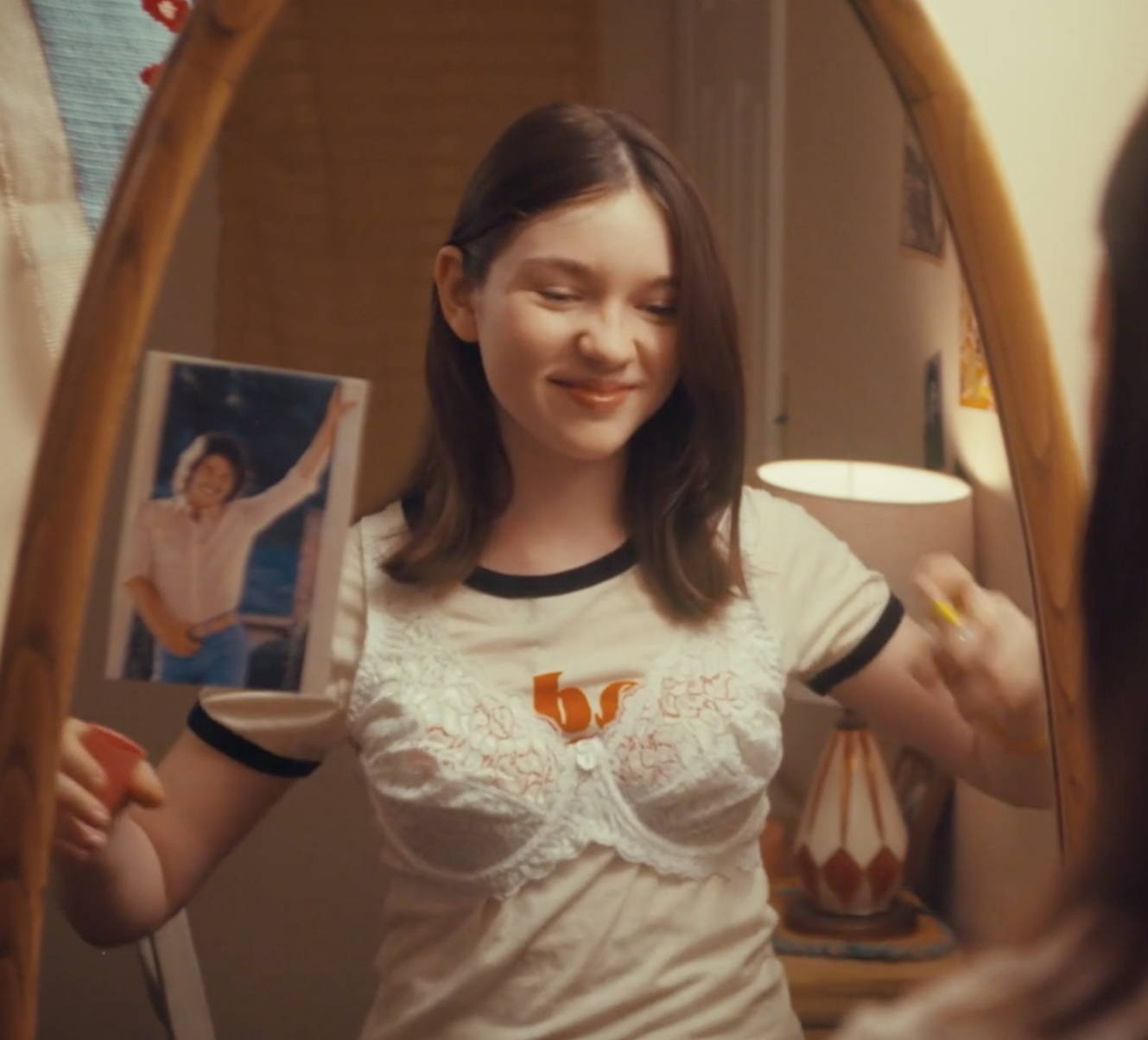 Young girl, smiling,  in front of mirror applying some Love's Baby Soft coologne on her. 