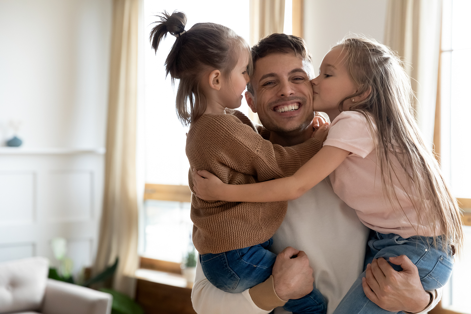 An attractive man holds his nieces in both his arms as they kiss his cheek and laugh together.