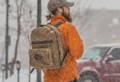 man in an orange sweater wearing a north bay daypack while its snowing