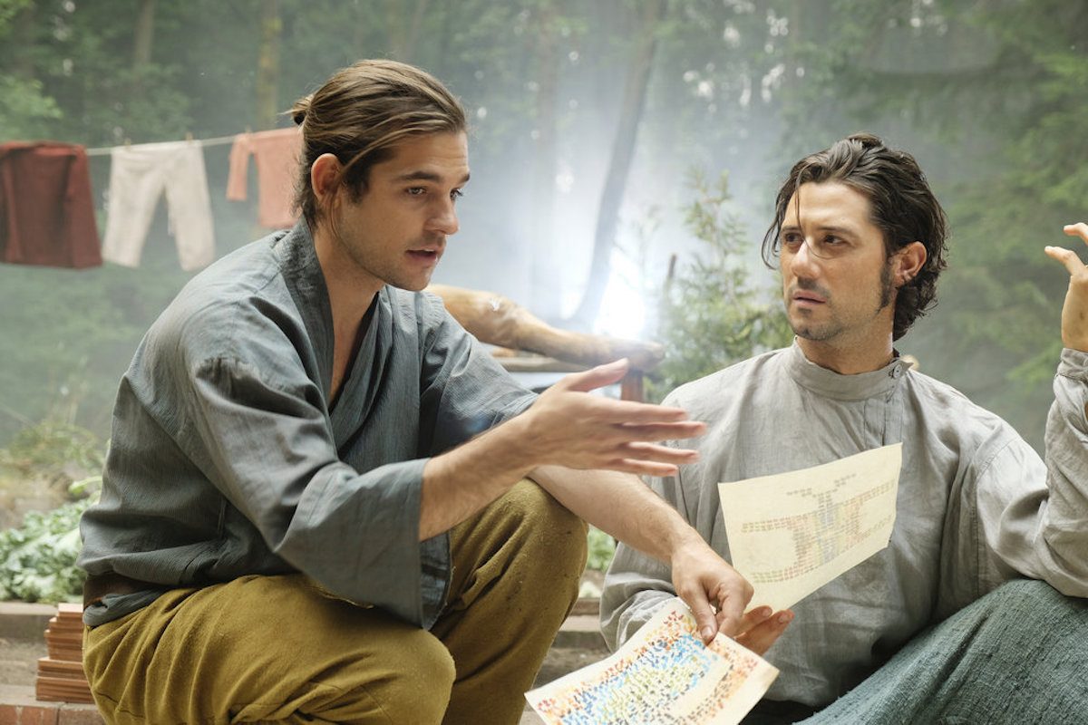 Quentin and Eliot discussing plans with a map, while out in the woods sitting on the ground.