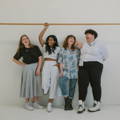 A diverse group of individuals laughing together and casually leaning against a white wall.