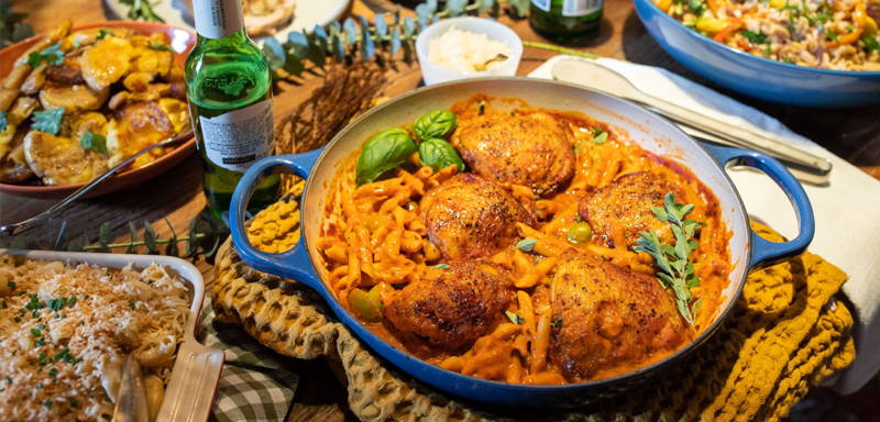 Table filled with dishes made of ZENB Pasta and Gourmet Pasta Sauce including hummus in a bowl, chicken in a skillet, a bread basket, pasta salad, green beans, and a sauced pork chop.