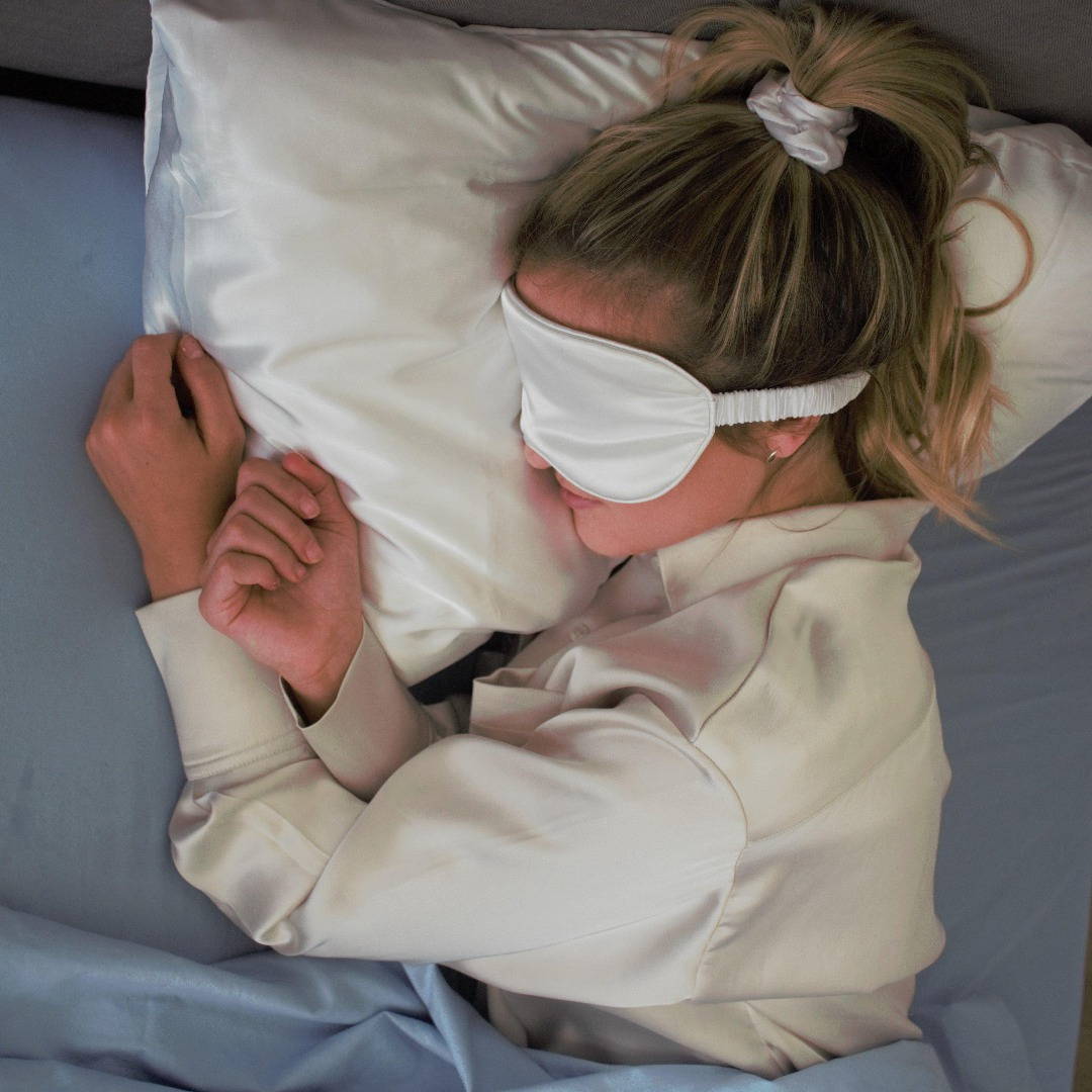 woman sleeping in bed wearing silk sleep mask and scrunchie.