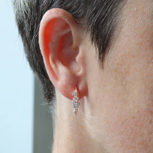 15 petits diamants sertis sur une boucle d'oreille anneau en or rose fixée sur l'oreille d'une femme.