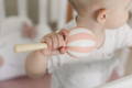 Baby holding a pink and white rattle while standing in her crib.