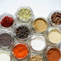 An overhead view of many glass spice jars with the lids off showing a variety of spices filling each one
