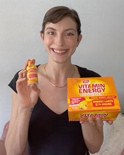 Woman smiling and holding a Vitamin Energy shot and box.
