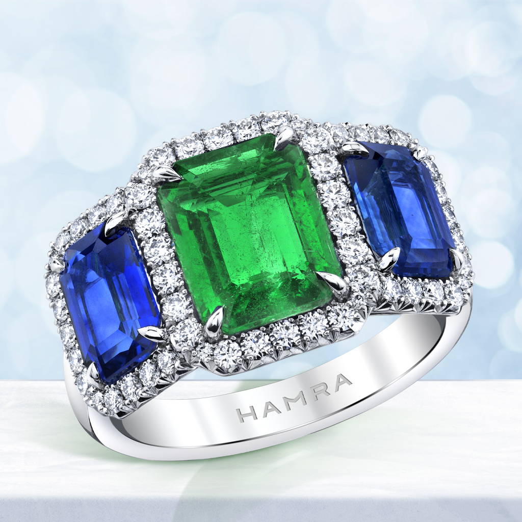 three stone ring featuring an emerald, two sapphires and diamond accents set in platinum