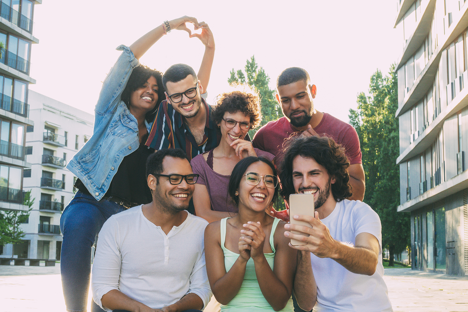 Photo of a group of multi ethnic attractive men and women grouped together trying to take a selfie. Someone made hearts with their hands, they are in a building area.