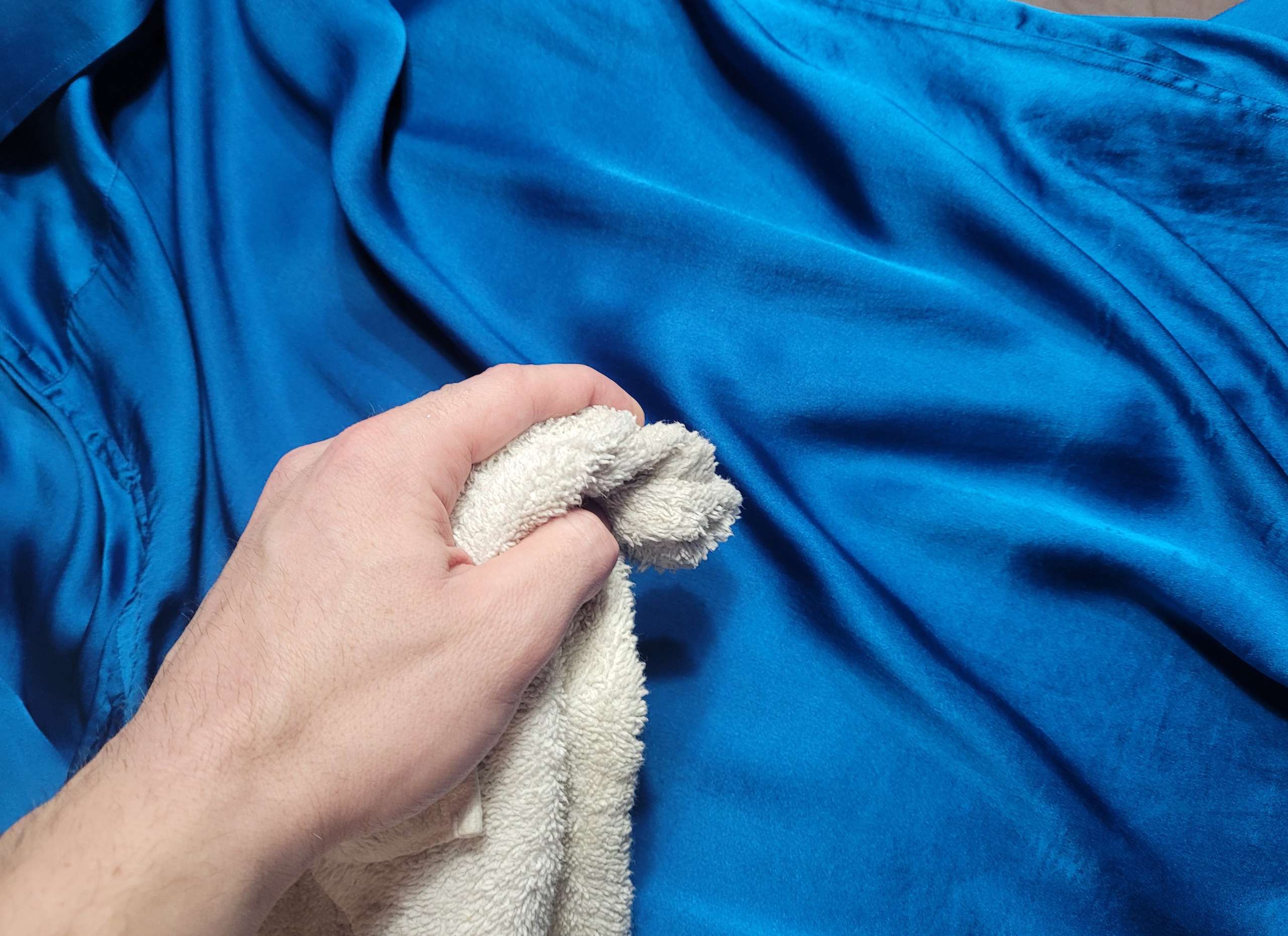 photo of a man using a damp white cloth to test a silk shirt for colorfastness