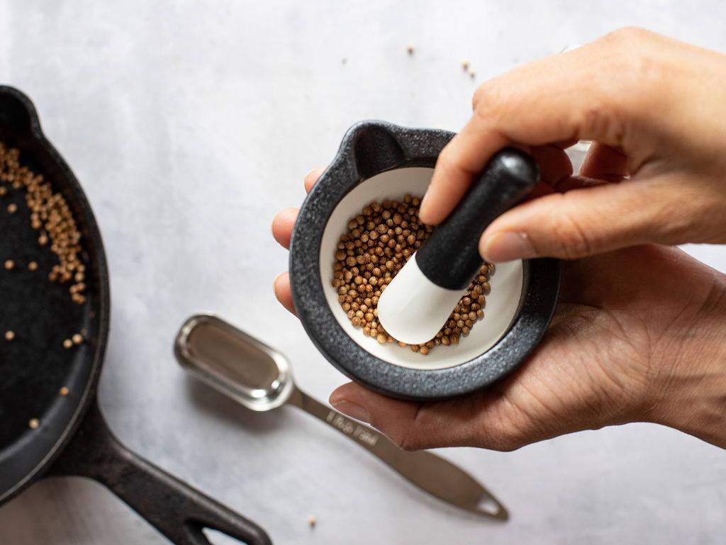Small spice seeds are crushed in a white and black mortar and pestle