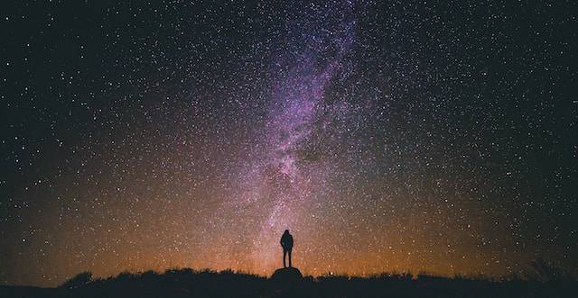 sagoma di un uomo che guarda la il cielo stellato di notte. Fotografato con la tecnica della lunga esposizione