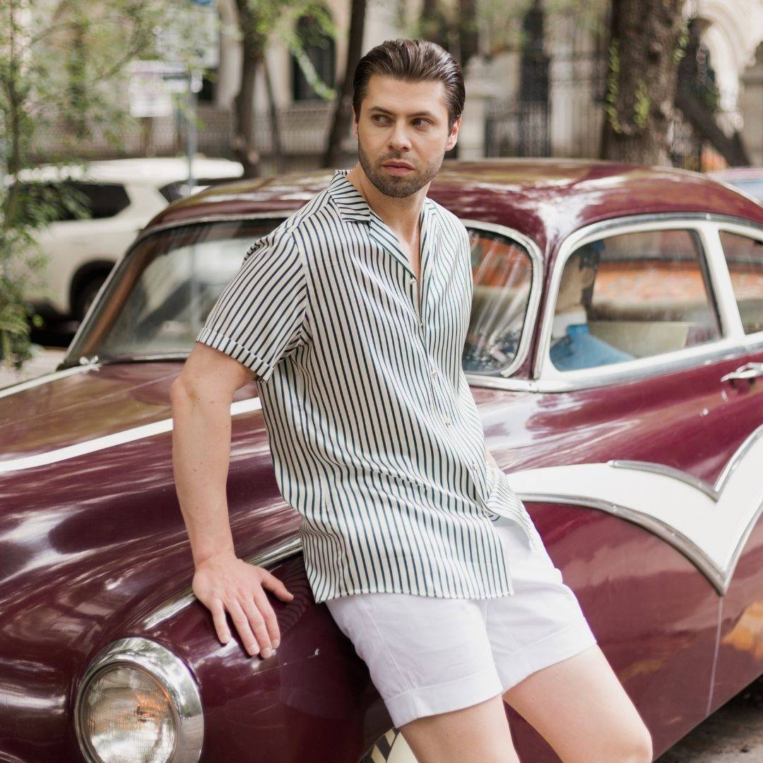 model leaning against a car wearing white shorts and a short sleeve green stripe shirt from 1000 kingdoms