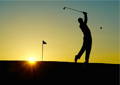 Silhouette of a golfer swinging a club at sunset near the flag.
