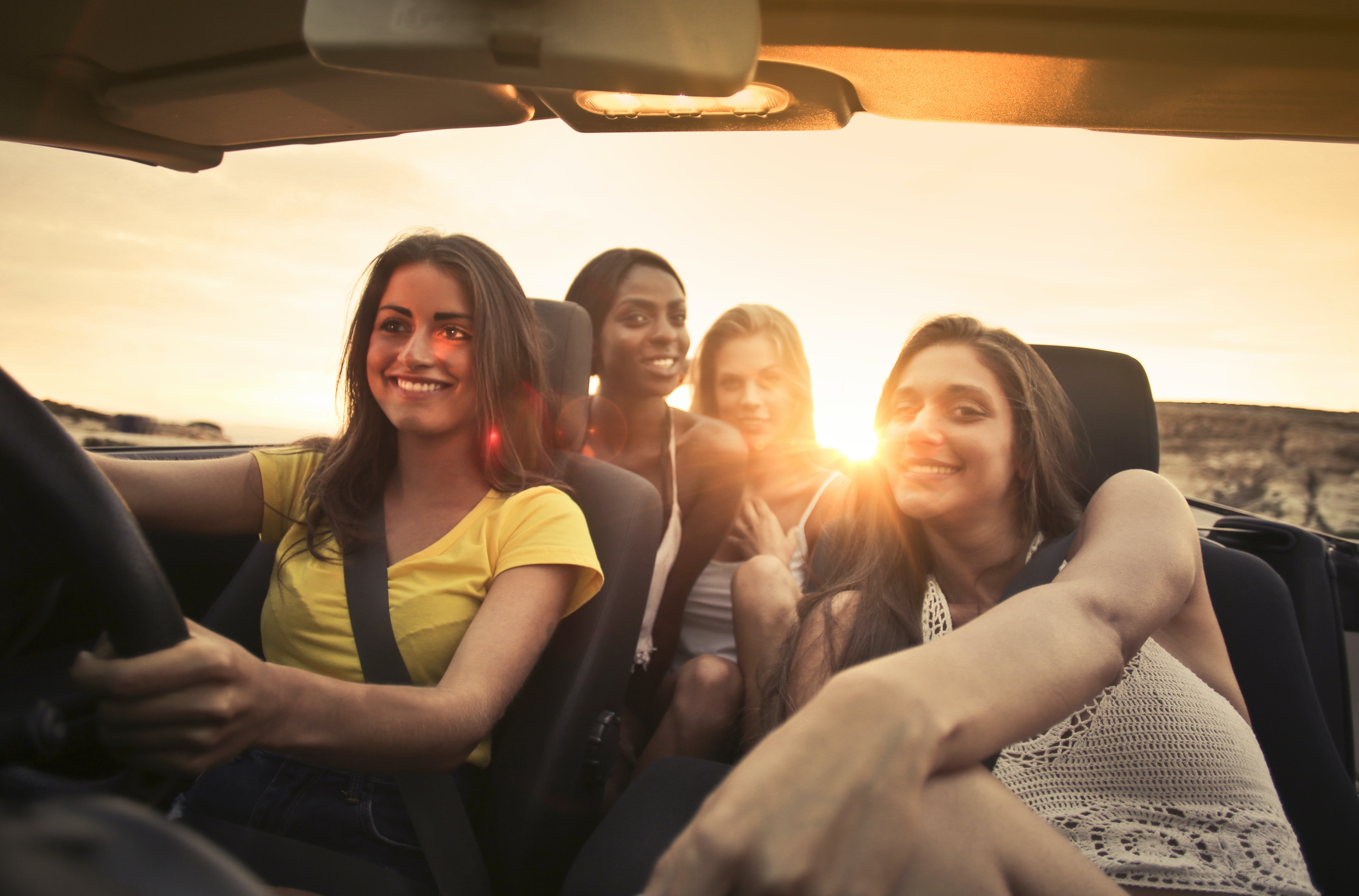 A group of 4 girlfriends driving at sunset smiling together.