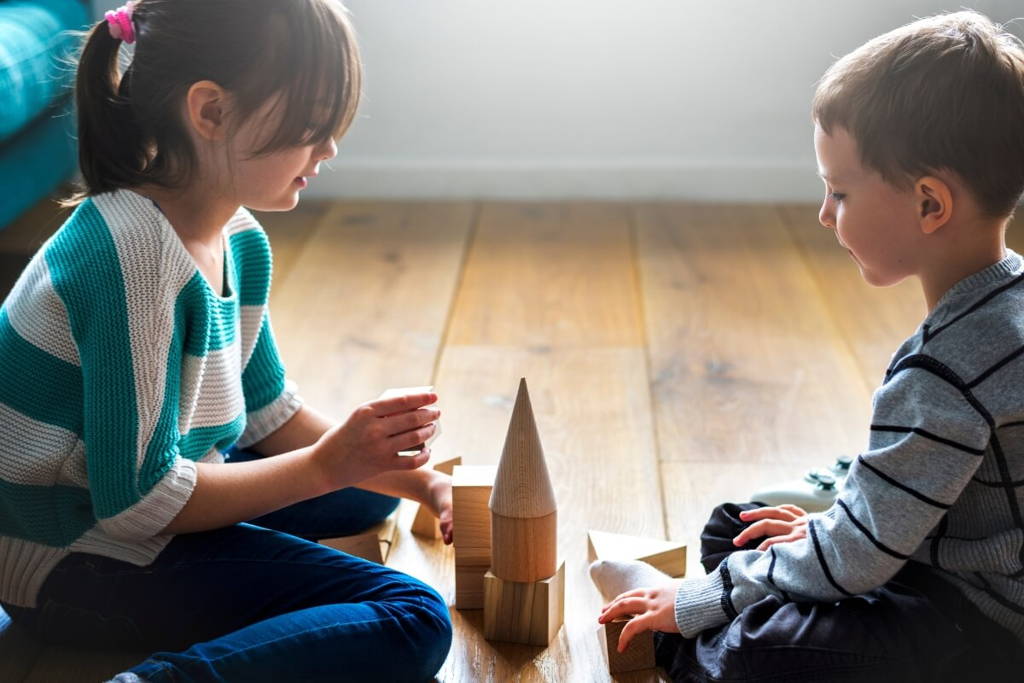 Brother and sister building a castle on the floor using wooden blocks and shapes.