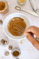A white bowl filled with various ground spices is being whisked to combine