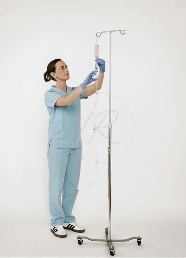 Medical worker in blue scrubs holding a microscope slide near a stand-mounted sample holder with tubing.