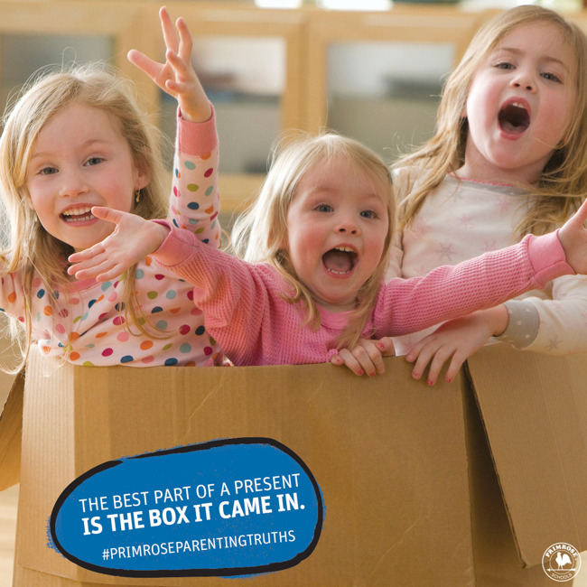 Three young girls stand inside a cardboard box and cheer with their arms up in the air