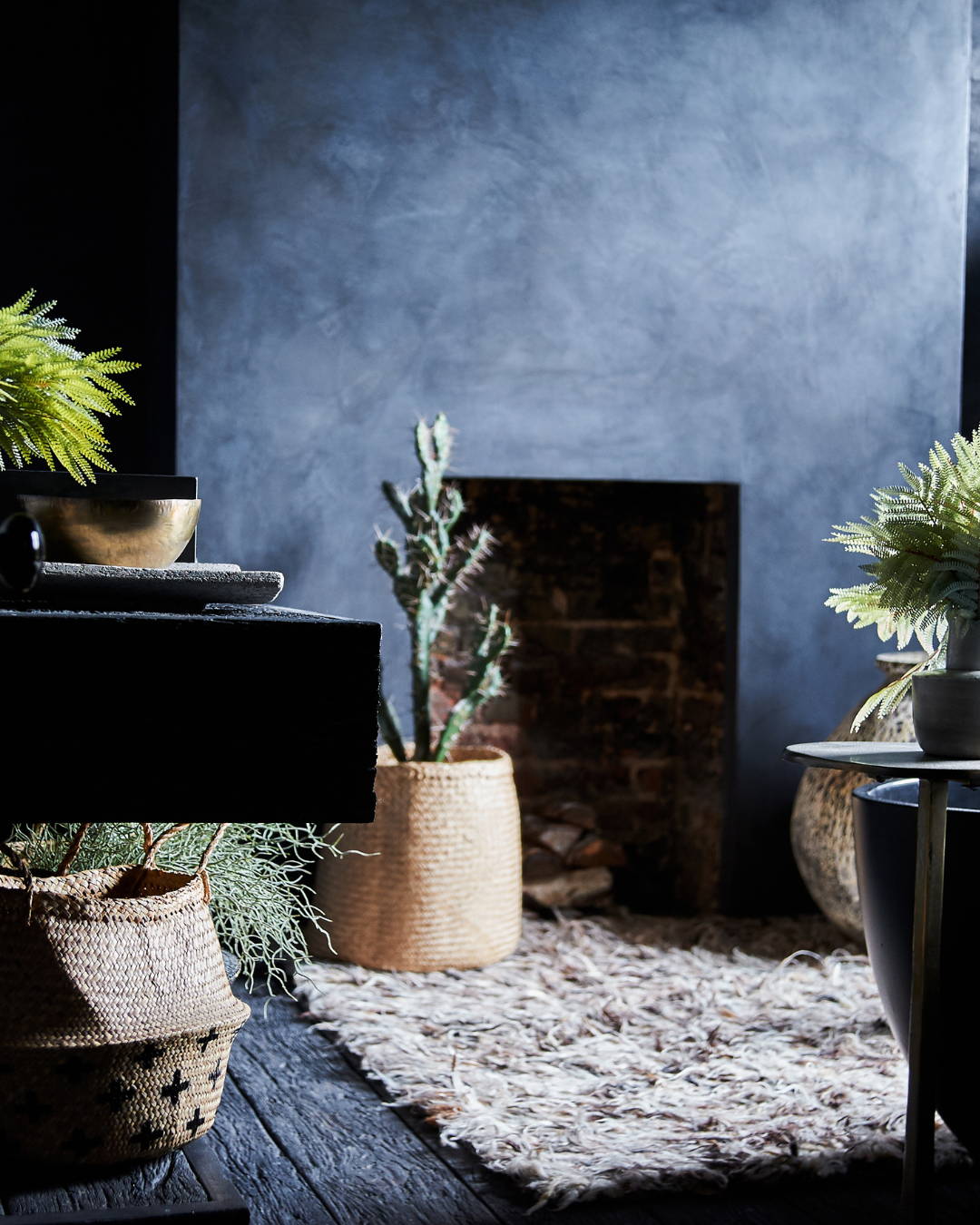 A dark bathroom with tadelakt walls, artificial plants in baskets and a shaggy wool rug