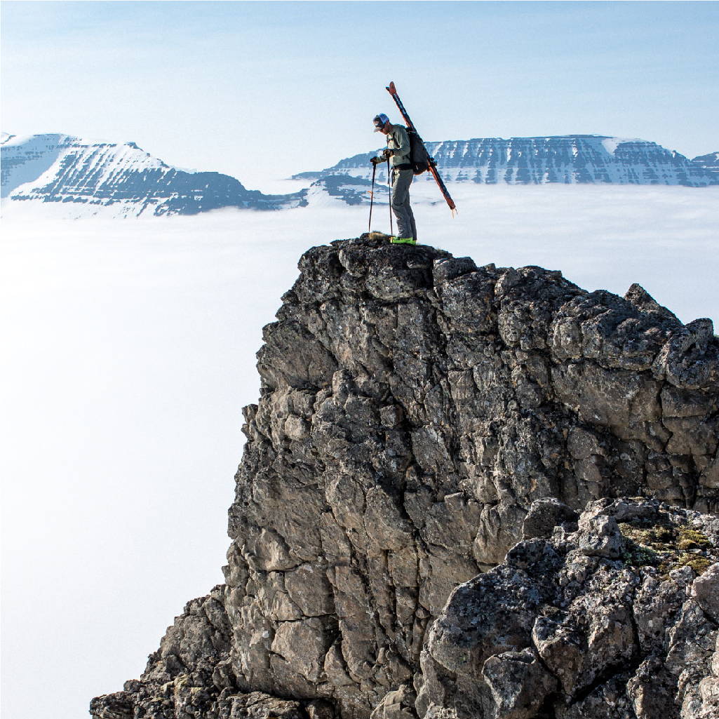 Man standing on top of a rocky cliff looking down at the snow