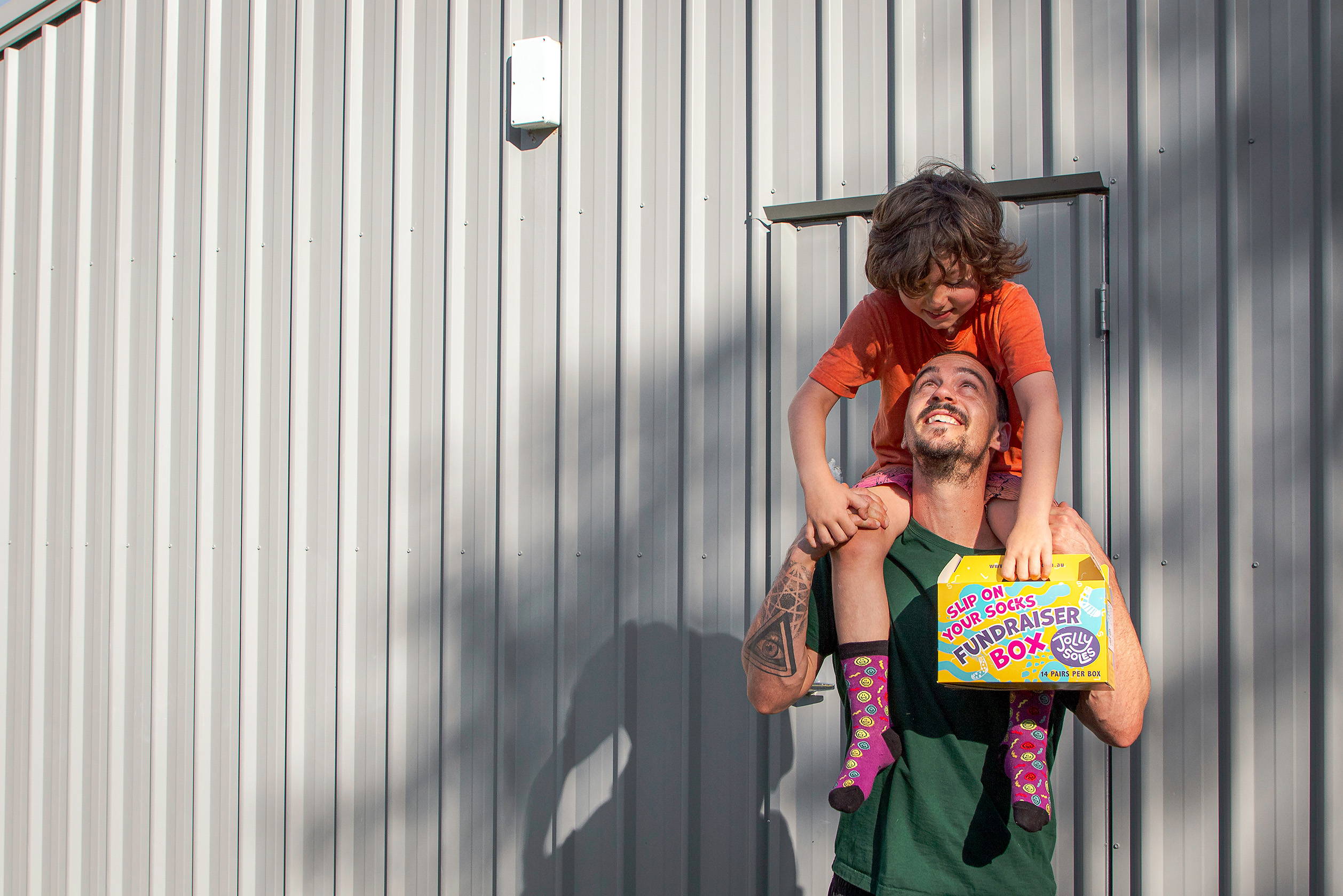 A dad with his son on his shoulders fundraising with a sock box.