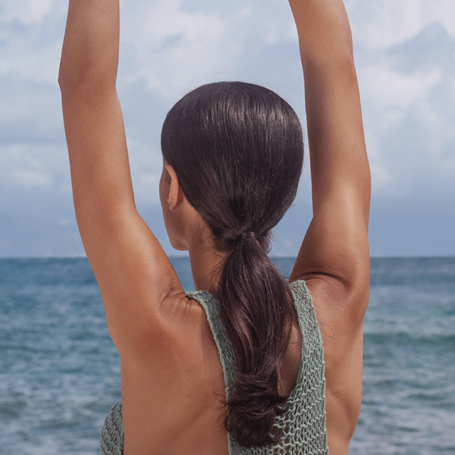 woman with a sleek, low brunette ponytail stretching her arms