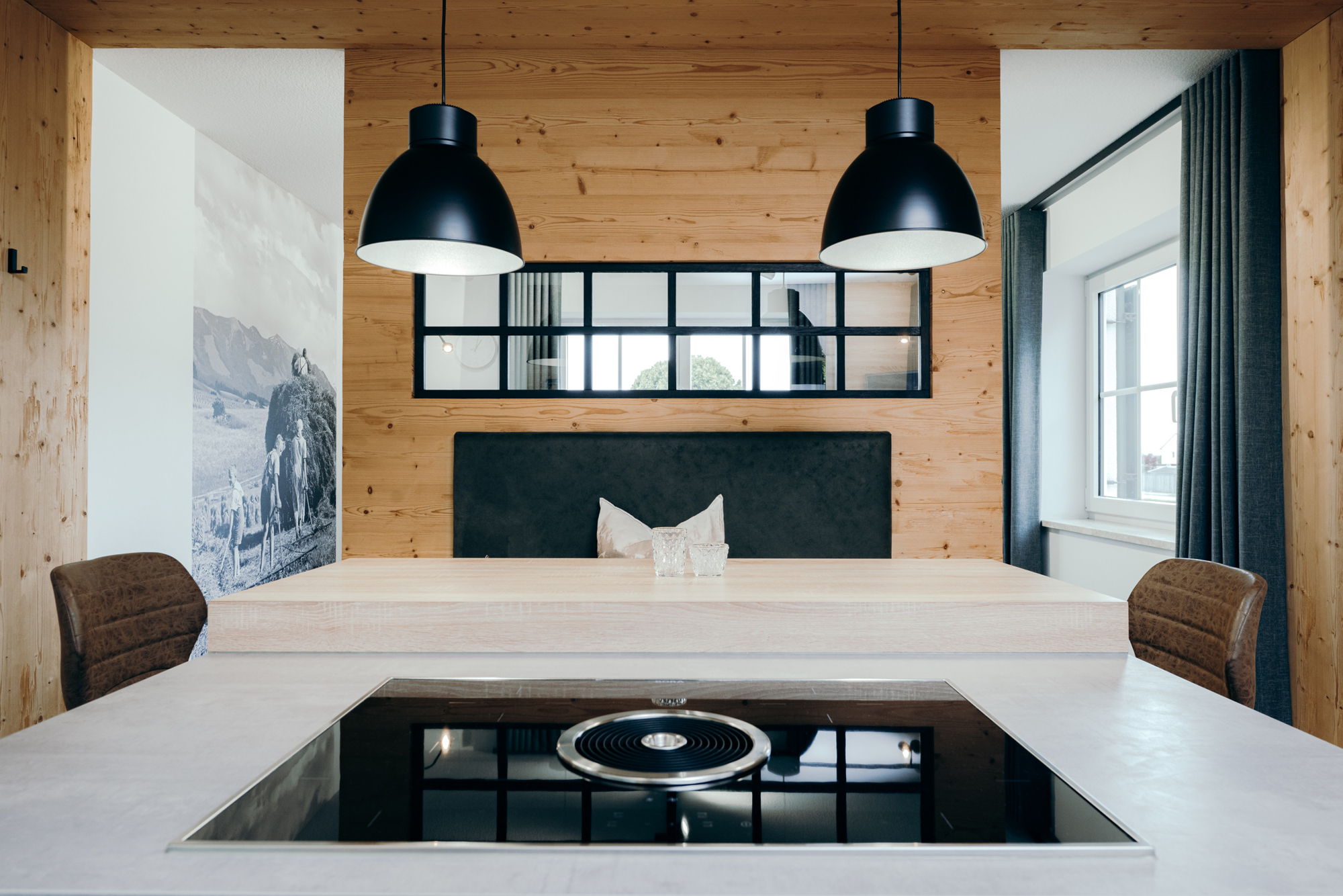 Ein hölzerner Essbereich mit hellem Esstisch, braunen Stühlen und schwarzen Deckenlampen.