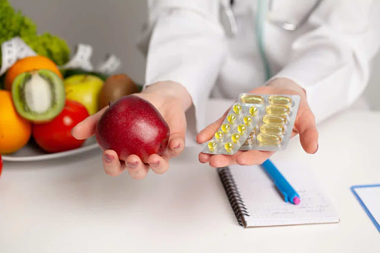 Nutritionist holding an apple and fish oil capsules, with fresh produce and notepad in the background.