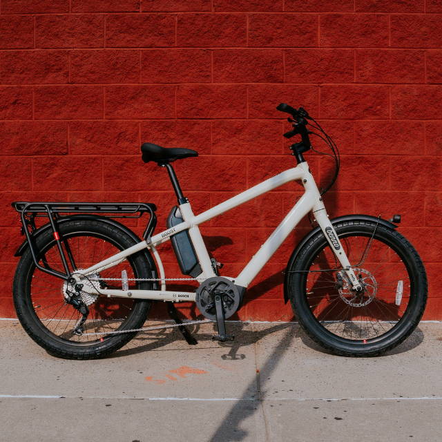 a a white benno boost electric cargo bike against a red brick wall