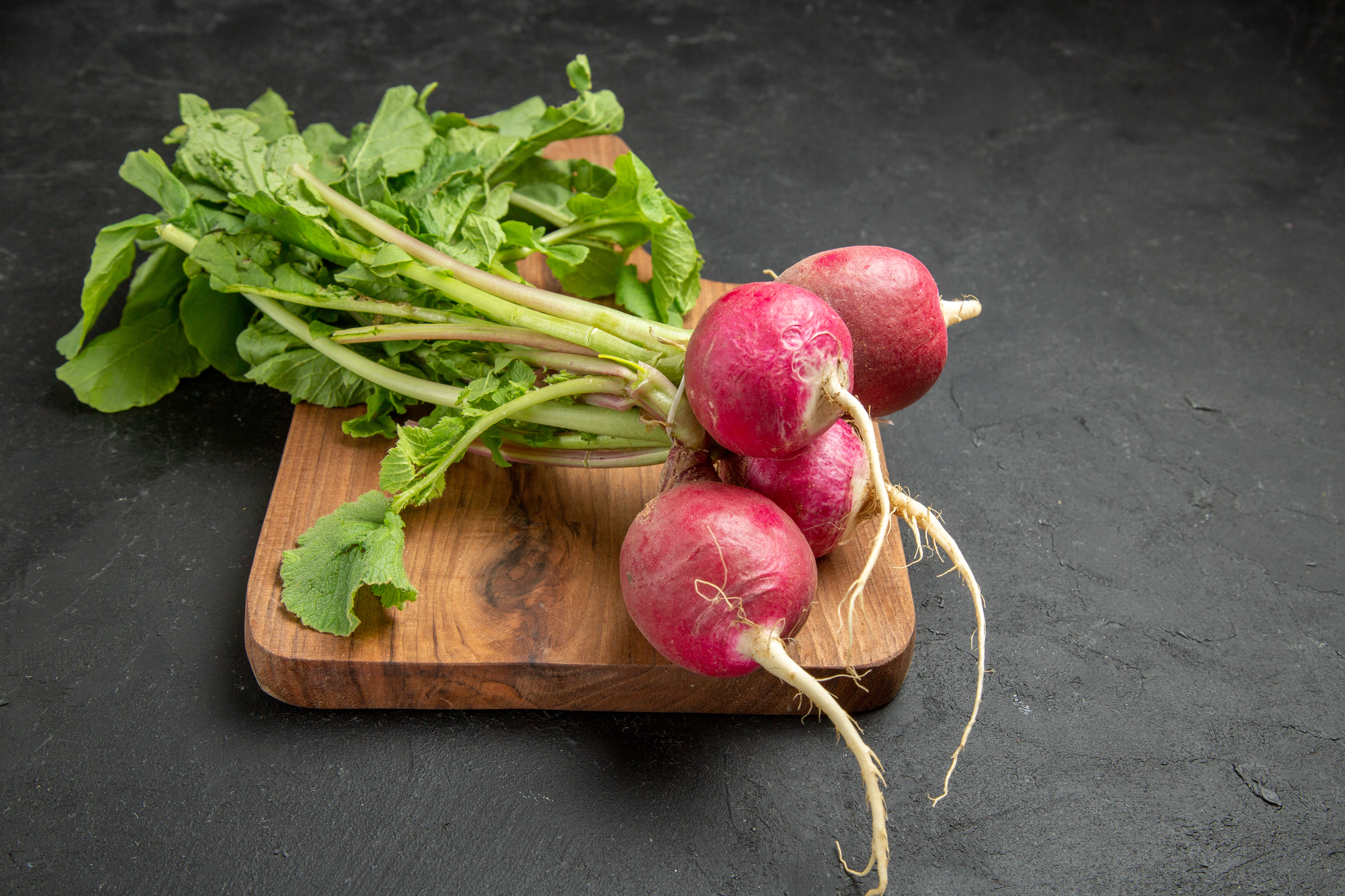 Pink radishes with leaves on a wooden cutting board with a slate background