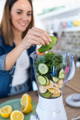 woman adding spinach, lemon, and cucumber to a blender