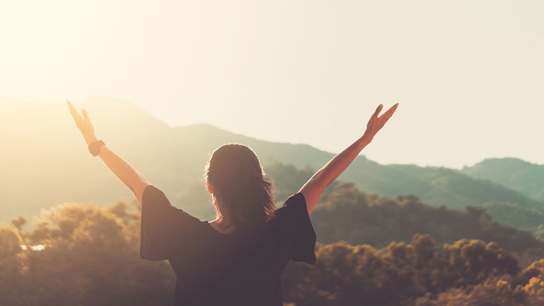 Earth Day - woman with raised hand on top of a mountain