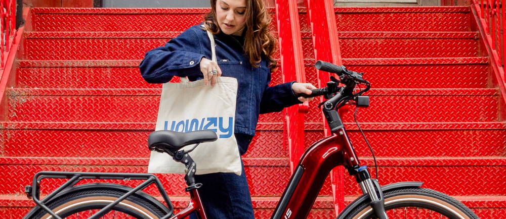 a woman standing next to an electric city bike while carrying an upway handbag