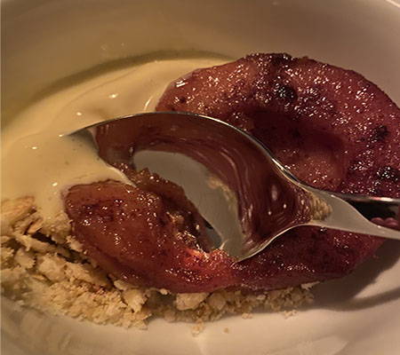A close of up a white bowl half-filled with a white-colored home made ice cream, glazed quince on a bed of cream-colored crumble and a spoon dipping into the quince.