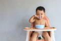 Little boy sitting on his lunch chair and eating with a spoon.