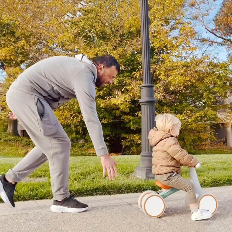 Father watching over his son while he is riding his baby bike in the park.