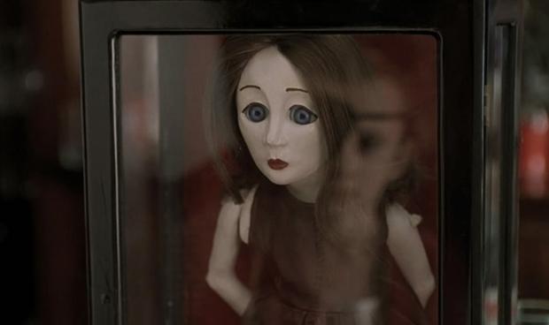 May's terrifying doll with pale skin, long brown hair, wide open eyes inside a glass case.