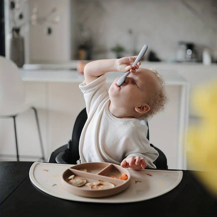 Cute baby eats with a spoon from the silicone First Bites Set.