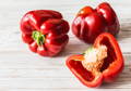 3 red peppers with one sliced on a wooden table