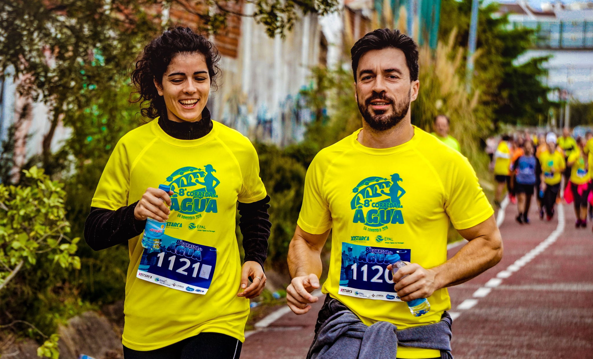 A multi ethnic older man and woman running on a track wearing numbers participating in a race.