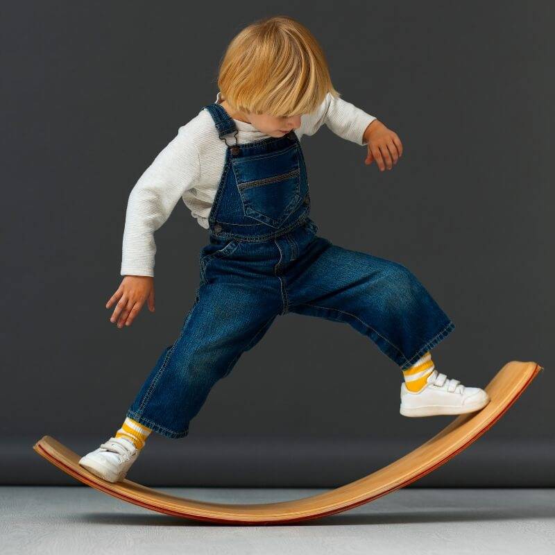 Boy swinging on a wooden Montessori balance board.