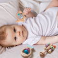 Baby laying in bed and holding its Montessori Rattle Toy.