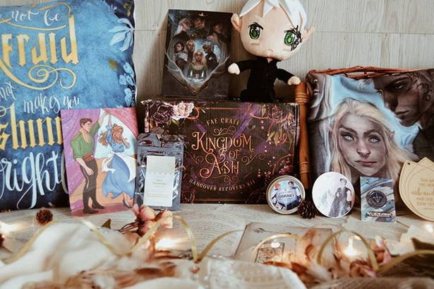 Kingdom of Ash Hangover box included Grumpy Fae Plushie, Double-Sided Sturdy Print, Heir of Fire Wooden Wall Hanger, Bromance Sticker and Candle Art, Bromance Candle, Court Blanket and Art Print, Maas Destruction Enamel Pin, and Chocolate Cake Drinking Chocolate