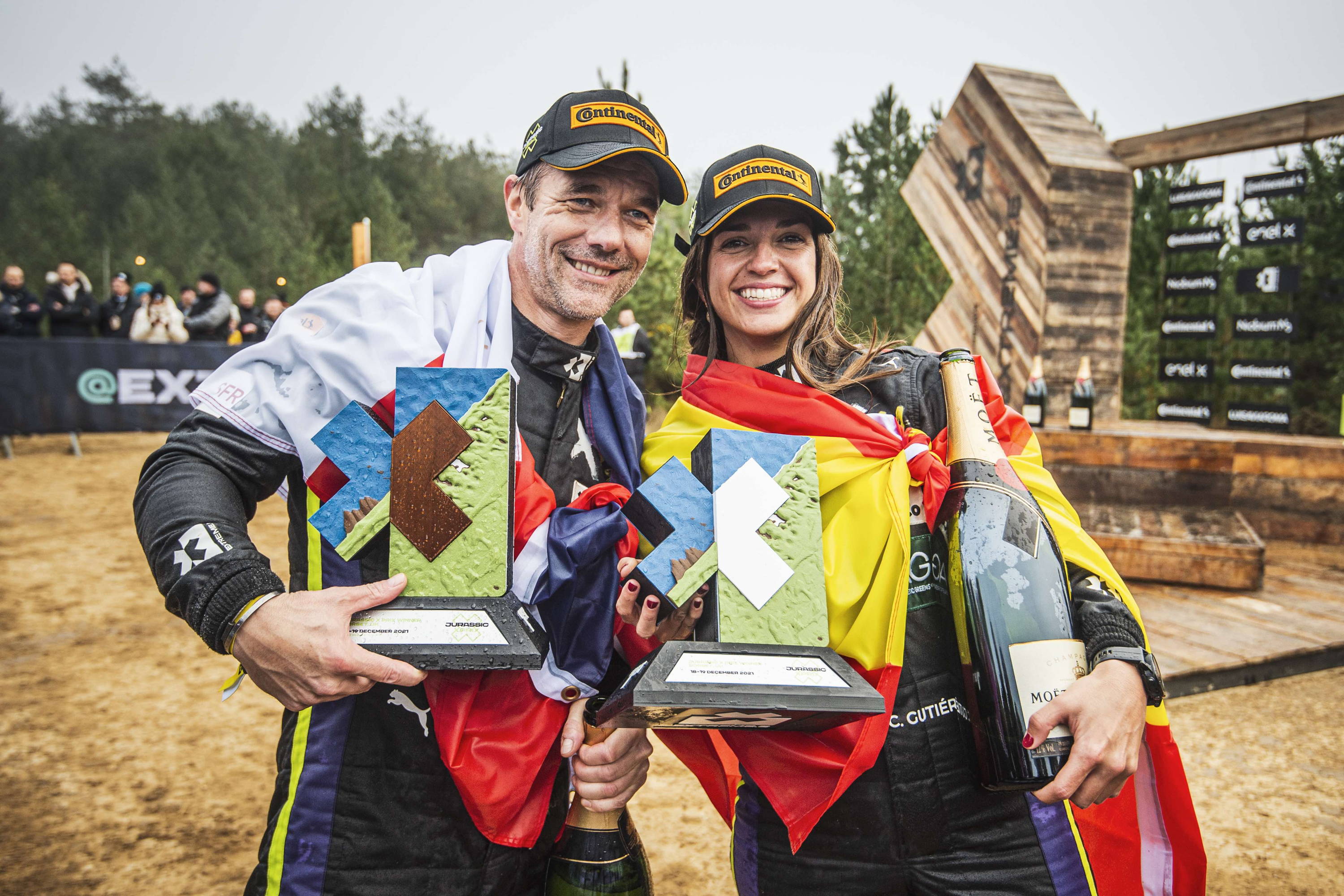 Electric racing car drivers Cristina Gutiérrez and Sébastien Loeb hold trophies after winning a race