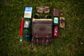 flat lay of a premium mesabi range daypack with an assortment of goods around it such as a hat, waterbottle, pocket folio and book.